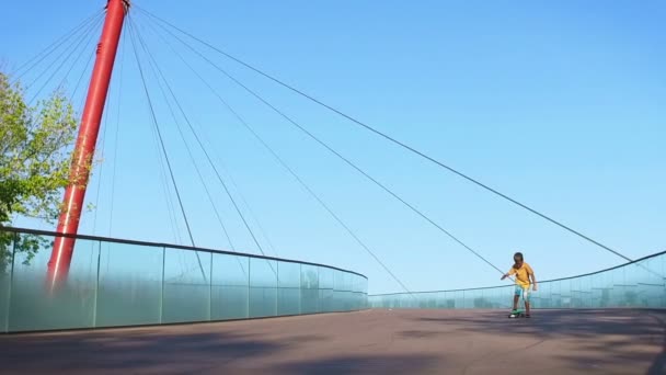 Criança, cruzando para baixo de uma ponte em um pennyboard, câmera lenta — Vídeo de Stock
