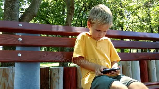 Niño jugando un juego en el teléfono móvil en el Parque — Vídeos de Stock