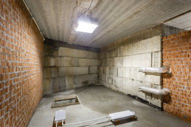 Büyük bir binanın bodrumunun beton yapısı. Zemin kat modern inşaat alanının içinde floresan ve doğal ışıkların karışımı. Çağdaş yapı beton ve tuğlalar duvarlar, sütunlar, tavan ve zemin