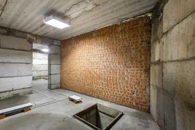 Büyük bir binanın bodrumunun beton yapısı. Zemin kat modern inşaat alanının içinde floresan ve doğal ışıkların karışımı. Çağdaş yapı beton ve tuğlalar duvarlar, sütunlar, tavan ve zemin