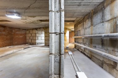 Büyük bir binanın bodrumunun beton yapısı. Zemin kat modern inşaat alanının içinde floresan ve doğal ışıkların karışımı. Çağdaş yapı beton ve tuğlalar duvarlar, sütunlar, tavan ve zemin