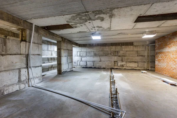 Büyük bir binanın bodrumunun beton yapısı. Zemin kat modern inşaat alanının içinde floresan ve doğal ışıkların karışımı. Çağdaş yapı beton ve tuğlalar duvarlar, sütunlar, tavan ve zemin