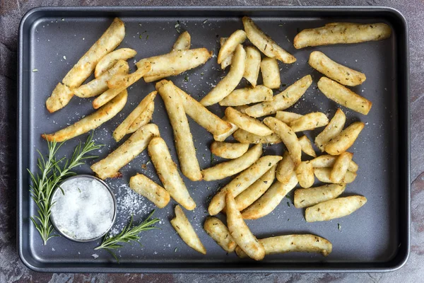 Kartoffelkeile mit Rosmarin und Meersalz von oben auf Backblech — Stockfoto