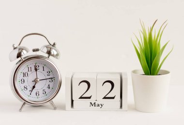 22 Mayıs 'ta ahşap bir takvimde çalar saat ve çiçeğin yanında. Bahar ayının bir günü, arka planda takvim ve çalar saat. Bahçede bahar. Yılda bir gün konsepti..