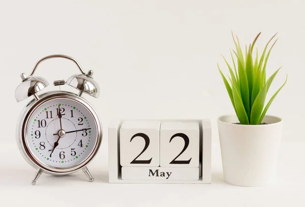 May 22 on a wooden calendar next to an alarm clock and a flower. One day of the spring month, calendar and alarm clock on a light background. Spring in the yard.The concept of one day a year.