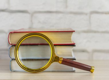 Masanın üzerinde bir yığın kitap ve bir büyüteç. Bilgi toplama kavramı..