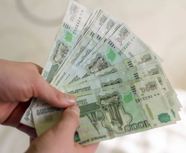 Dinero ruso.Un joven sostiene billetes con un valor nominal de 1000 rublos.Mucho dinero en la mano, primer plano . — Foto de Stock