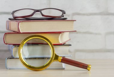 Masanın üzerinde bir yığın kitap, gözlük ve büyüteç. Bilgi araması kavramı..