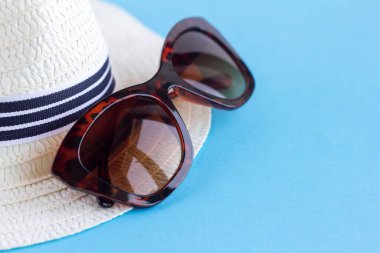 Orijinal çerçeveli güneş gözlüğü ve mavi arkaplanda beyaz bir şapka..