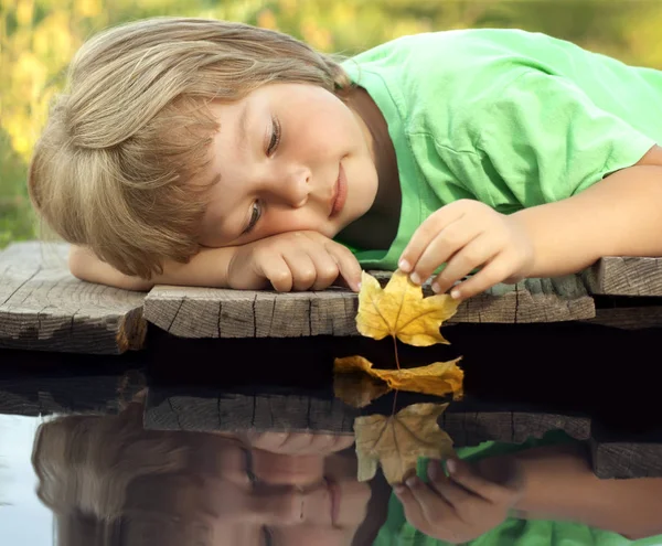 Pojke spela med höstens löv fartyg i vatten, chidren i park spela wi — Stockfoto