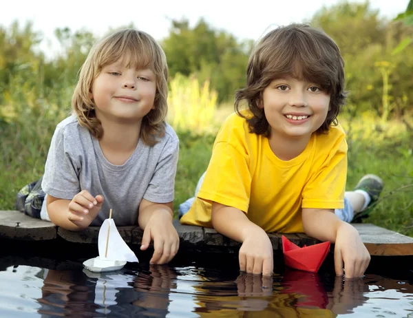 Two boys allowed paper boats from the pier of river — Stock Photo, Image
