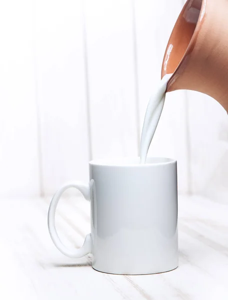 Melk wordt gegoten in een kopje werper op witte achtergrond houten — Stockfoto