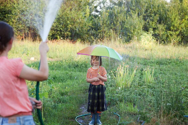 Moeder haar zoon met een slang paraplu spelen in de regen te drenken — Stockfoto