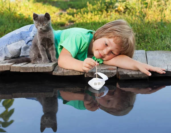 Menino e seu gatinho amado brincando com um barco do cais na lagoa — Fotografia de Stock