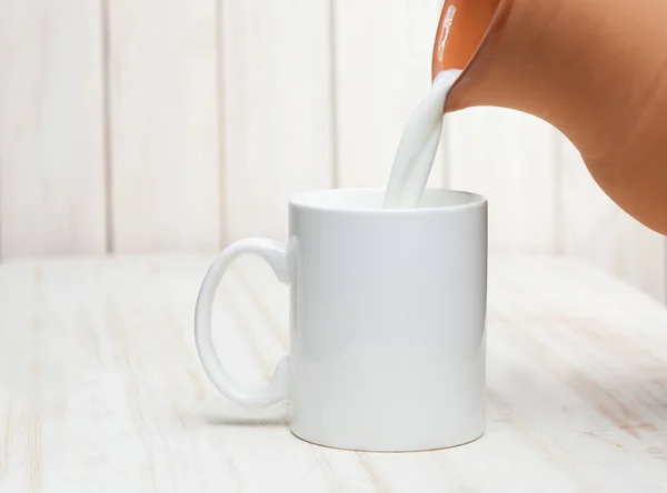 Молоко наливают в чашку кувшин на белом фоне деревянный — стоковое фото