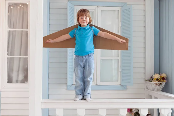 Happy boy with cardboard boxes of wings in home dream of flying — Stock Photo, Image