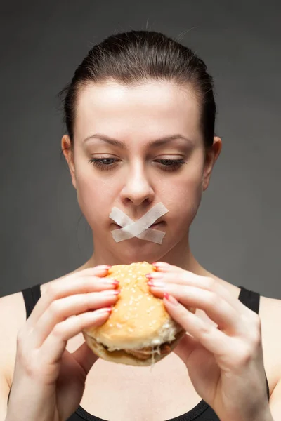 Dieet concept: vrouw met een hamburger met mond verzegeld — Stockfoto