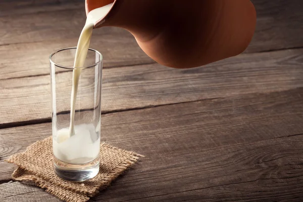 Jarra de leche con una mesa de campo viejo, una bebida blanca se vierte i — Foto de Stock