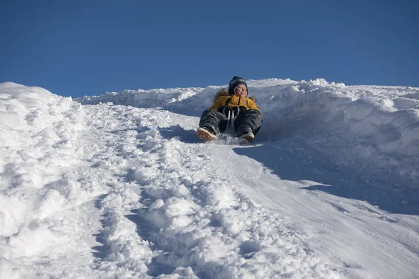 Glücklicher Junge, der im Winter auf dem Schlitten den Schneehügel hinuntergleitet, — Stockfoto