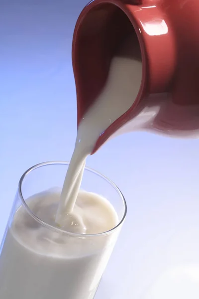 Melk gegoten uit een rode kan in glas op blauwe achtergrond isoleren — Stockfoto