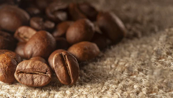 Roasted Black coffee beans on Burlap Sack background. Aroma ingr — Stockfoto
