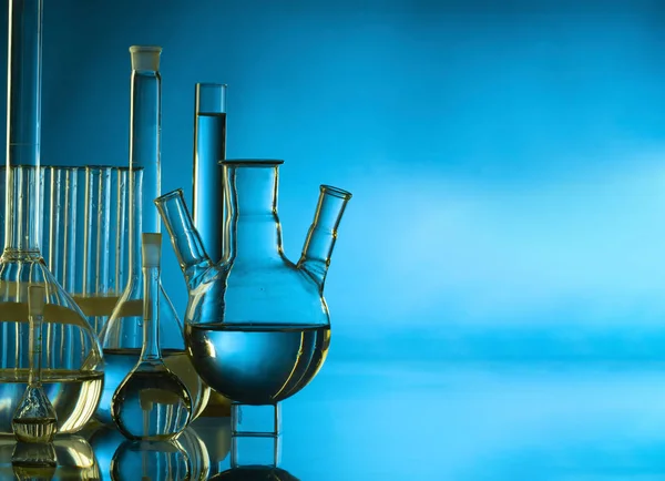 Retort flask on glass table with blue liquid on table against bl — Stock Photo, Image