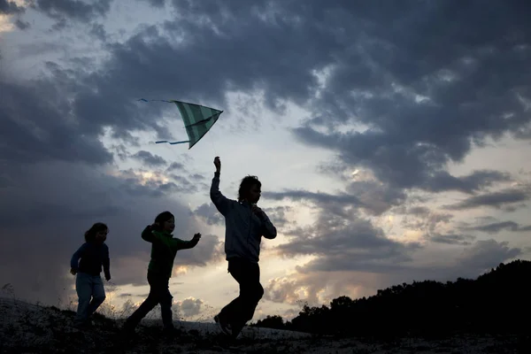 Les enfants courent avec cerf-volant sur la silhouette de prairie de coucher de soleil d'été. jouer — Photo