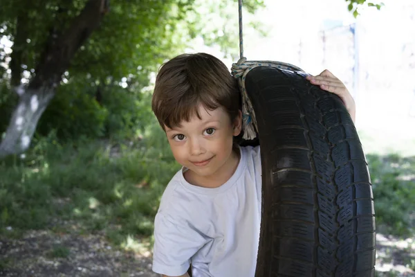Happy Boy jugando en una rueda basculante en el jardín. Soleado verano d —  Fotos de Stock