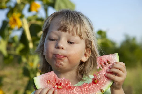 Счастливый ребенок ест арбуз в саду. Мальчик с фруктами на открытом воздухе — стоковое фото