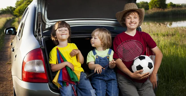 Trois enfants joyeux assis dans le coffre d'une voiture sur la nature — Photo