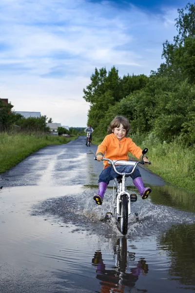 Rower w parku przejeżdża przez kałużę w deszczowe dni. Chłopiec na bi — Zdjęcie stockowe