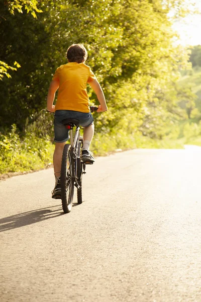 Adolescente montando una bicicleta en el camino verano soleado — Foto de Stock