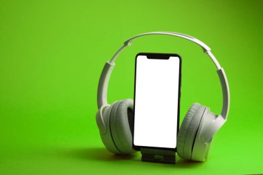 Akıllı telefon modeliyle beyaz kulaklıklar, turuncu ile izole edilmiş, çevrimiçi müzik konsepti.