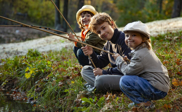 Happy boys go fishing on the river, 3 children of the fisherman with a fishing rod on the shore of the lake