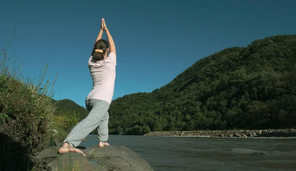 年轻女子正在高山湖畔练习瑜伽 姿势是 勇士之池 Virabhadrasana — 图库照片