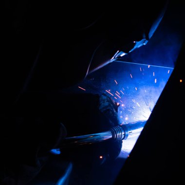 Maskeli kaynakçı, metal kaynaklama fabrikasında çalışıyor. Kıvılcım ve 