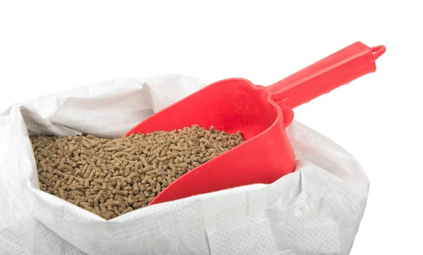 Red scoop inserted in a bagful of pelleted horse feed, isolated on white — Stock Photo, Image