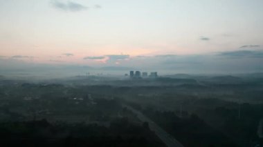 Şehir dağlarda, sis altında gün batımında. 