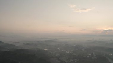 Şehir dağlarda, sis altında gün batımında. 