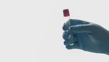 Doktorun elinde kırmızı bir sıvı tutuyor.