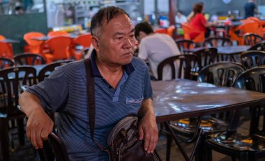 Olgun bir adam masada oturuyor ve kameraya bakıyor.