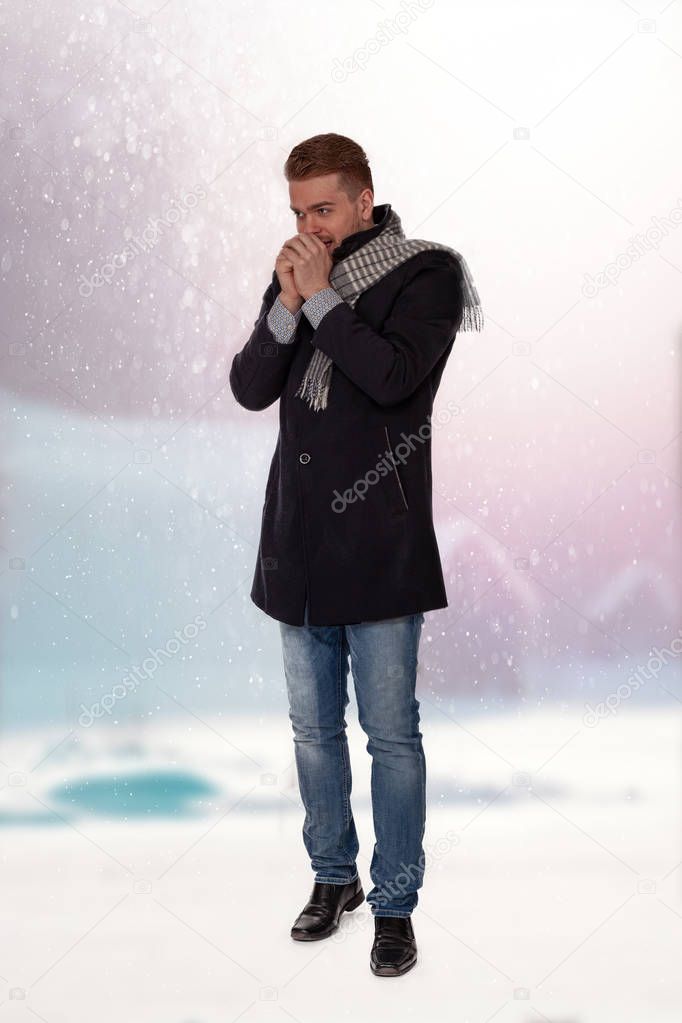 Fashionably dressed man holds his cold hands over his mouth and blows in