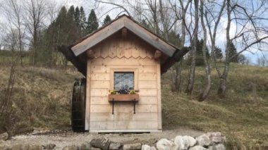 Doğada küçük su değirmeni çiçek kutusu ve arka planda çanlar var.