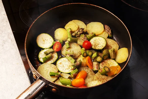 Pan on a hotplate with potatoes, zucchini, small vine tomatoes and green asparagus
