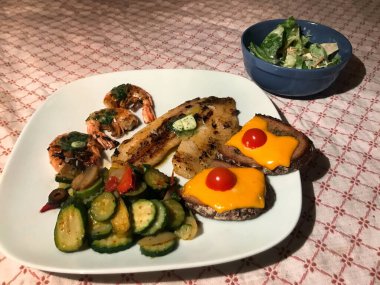 Izgara ciklet fileto, bitkisel tereyağı, karides, Akdeniz sebzesi ve ızgara sarımsaklı ekmek ve yanında salata.