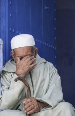 : Chefchaouen, Morocco mavi bir kapı önünde oturan adam.