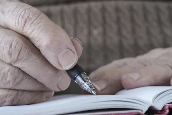 Mão enrugada escrevendo nota com lápis — Fotografia de Stock
