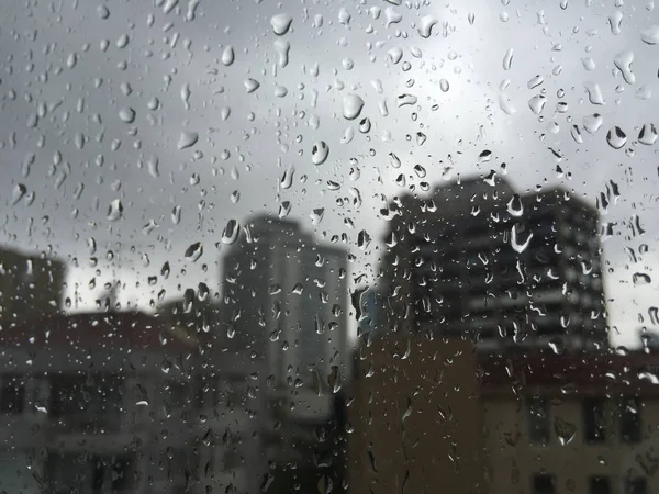 Gotas de lluvia en el cristal de la ventana contra los edificios — Foto de Stock