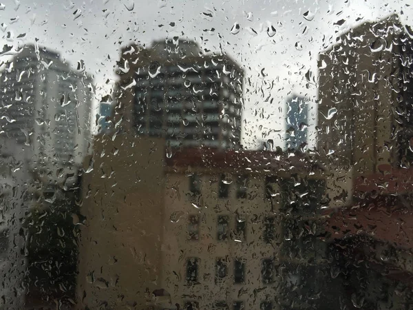 Binalar karşı pencere camı üzerinde yağmur damlaları — Stok fotoğraf