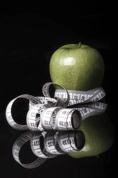 A green apple and measuring tape on black with reflection